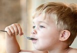 Ein blonder Junge ist Joghurt mit einem Löffel. | © gettyimages.de / Becki Bennett