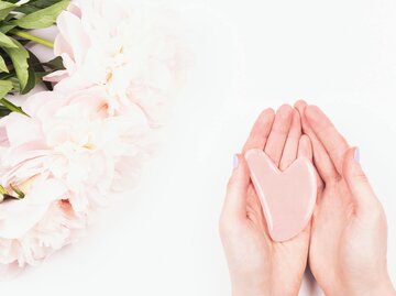 Frau hält Gua Sha Stein aus Rosenquarz in ihren Händen. | © gettyimages.de | Yulia Lisitsa