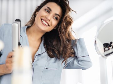  Junge Frau macht sich Locken mit einem Glätteisen | © Getty Images/	YakobchukOlena