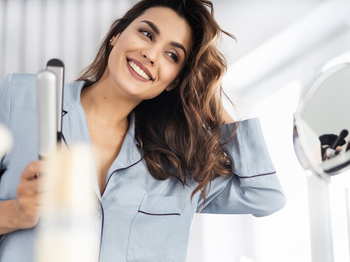  Junge Frau macht sich Locken mit einem Glätteisen | © Getty Images/	YakobchukOlena