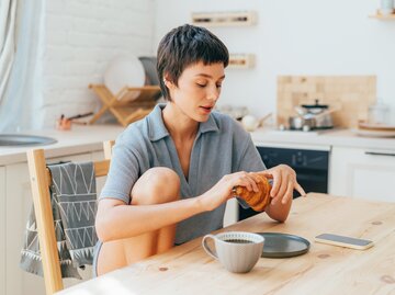 Frau sitzt am Frühstückstisch und isst Croissant | © Getty Images/	ilona titova