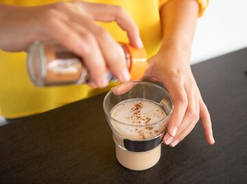 Frau macht sich eine Prise Zimt in ihren Kaffee | © Getty Images/	Gonçalo Barriga