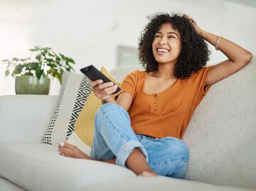 Junge Frau sitzt entspannt auf der Couch und guckt Feel Good Serie | © Getty Images/	LaylaBird