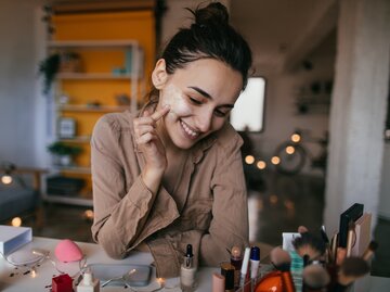 Frau sitzt am Schminktisch und blickt auf ihre Beauty-Produkte | © Getty Images/	AleksandarNakic