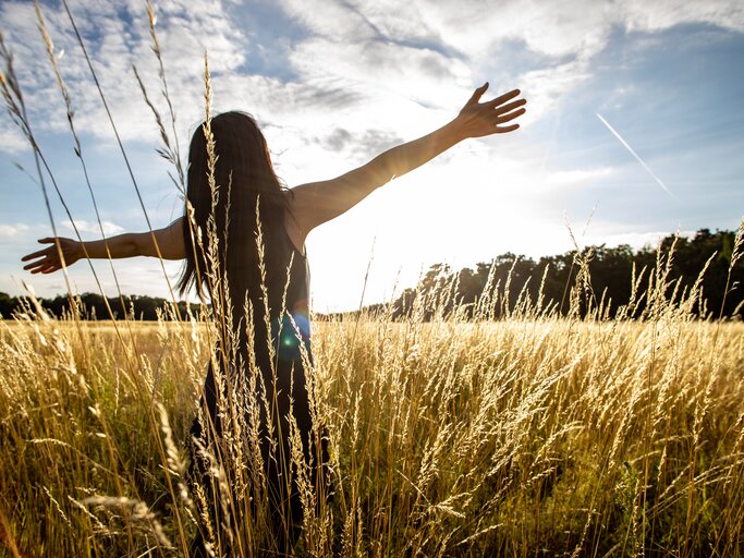 Frau streckt ihre Arme auf einem Feld aus | © Getty Images/	Rick Neves