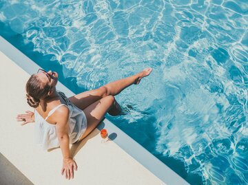 Frau sitzt glücklich und gelassen am Pool | © Getty Images/	Sviatlana Barchan