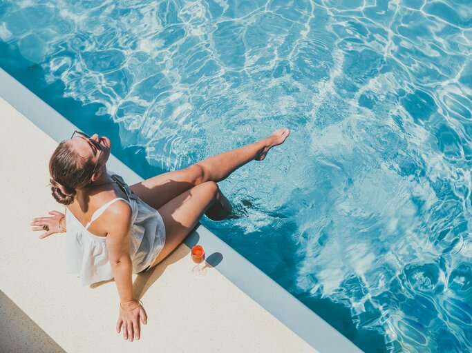 Frau sitzt glücklich und gelassen am Pool | © Getty Images/	Sviatlana Barchan