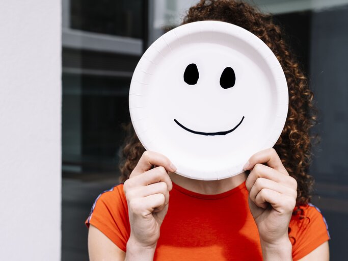 Frau hält sich ein Bild mit Smiley vors Gesicht | © Getty Images/	Westend61