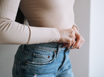 Frau knöpft sich die Jeans zu, die zu eng ist | © Getty Images/	Galina Zhigalova