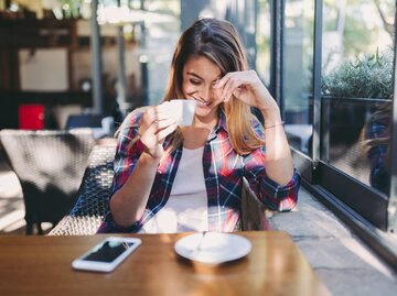 Schüchterne Frau sitzt lächelnd im Café | © Getty Images/martin-dm