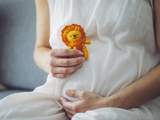 Schwangere Frau hält sich Löwe-Kuscheltier vor den Bauch | © Getty Images/Eva-Katalin