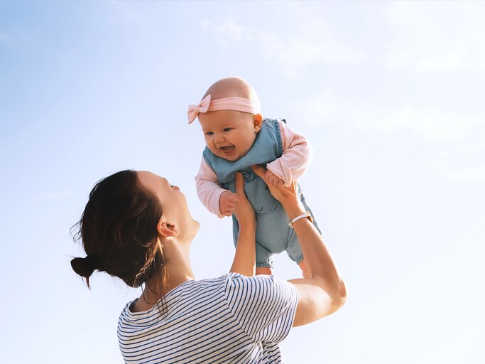 Frau hebt ihr Baby in die Luft und lacht | © Getty Images/	NataliaDeriabina