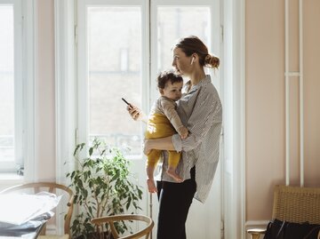 Frau hat Kind im Arm und guckt aufs Handy | © Getty Images/Maskot