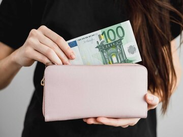 Frau packt 100 Euro Schein in Geldbeutel | © GettyImages/nikkimeel