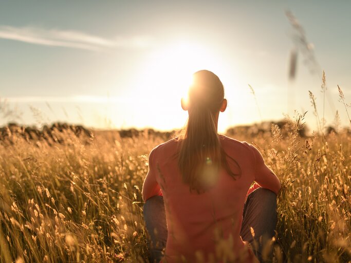 Frau sitzt im Feld | © Adobe Stock