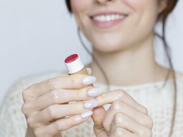 Frau trägt Lippenpflegestift auf | © GettyImages/Lourdes Balduque