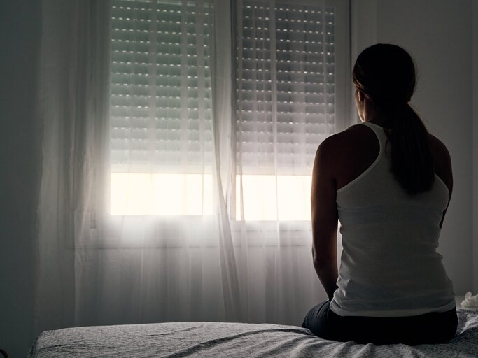 Frau sitzt in Dunkelheit im Schlafzimmer | © GettyImages/	Alvaro Medina Jurado