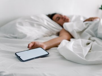 Frau liegt im Bett und hält Smartphone-Wecker in der Hand | © AdobeStock/phpetrunina14