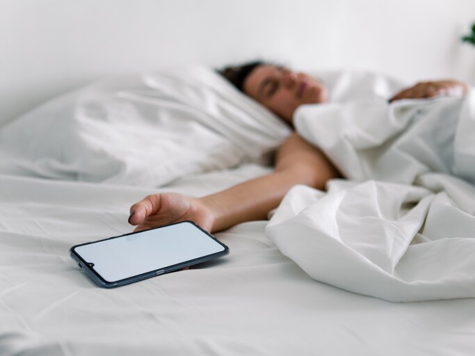 Frau liegt im Bett und hält Smartphone-Wecker in der Hand | © AdobeStock/phpetrunina14