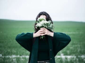 Frau versteckt ihr Gesicht hinter Blumenstrauß | © GettyImages/Alexey Karamanov