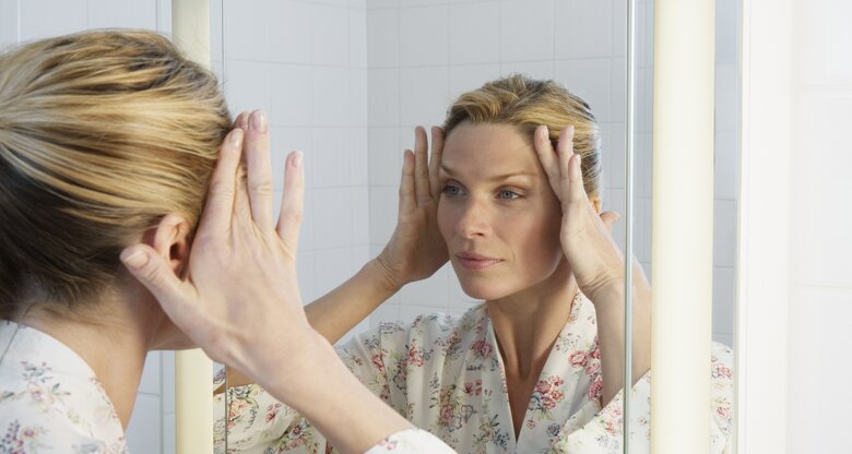 Frau blickt kritisch in den Spiegel | © GettyImages/Robert Decelis