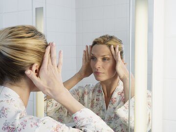 Frau blickt kritisch in den Spiegel | © GettyImages/Robert Decelis