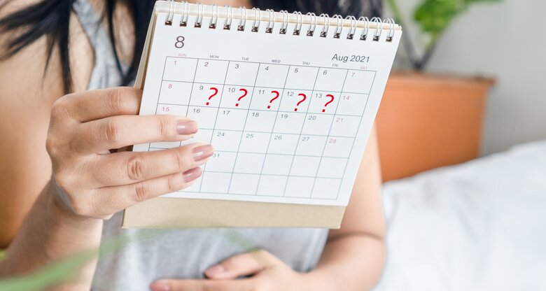 Frau hält sich ihren Bauch und blickt auf Kalender, weil ihre Periode zu spät ist | © GettyImages/Doucefleur