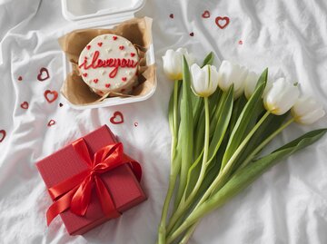 Tulpen, Geschenk und süße Valentinstags-Torte auf dem Bett angerichtet | © GettyImages/Alexandr Kolesnikov