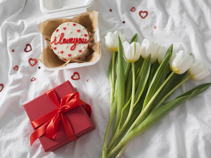 Tulpen, Geschenk und süße Valentinstags-Torte auf dem Bett angerichtet | © GettyImages/Alexandr Kolesnikov