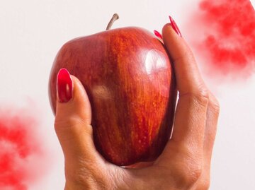 Rote Fingernägel halten einen Apfel umklammert | © GettyImages/	infinitusstudios