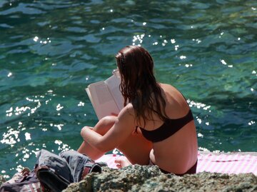 Frau liest ein Buch auf einer Klippe am Meer | © GettyImages/	EyeEm Mobile GmbH