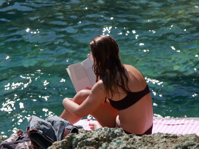 Frau liest ein Buch auf einer Klippe am Meer | © GettyImages/	EyeEm Mobile GmbH