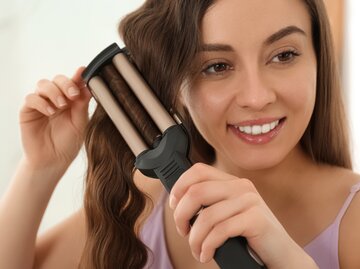 Junge Frau stylt sich die Haare mit einem Welleneisen | © ©shutterstock/New Africa