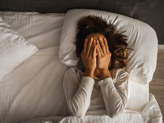 Frau liegt im Bett und hält sich die Hände vor das Gesicht | © Getty Images/Oleg Breslavtsev