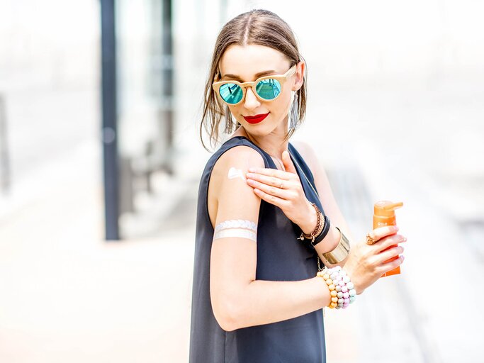 Frau cremt sich mit Sonnencreme ein | © Getty Images/RossHelen