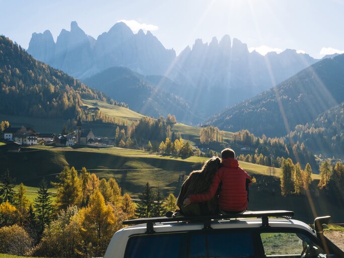 Paar sitzt auf dem Auto und blickt in herbstlichen Wald | © Getty Images/Ascent/PKS Media Inc.