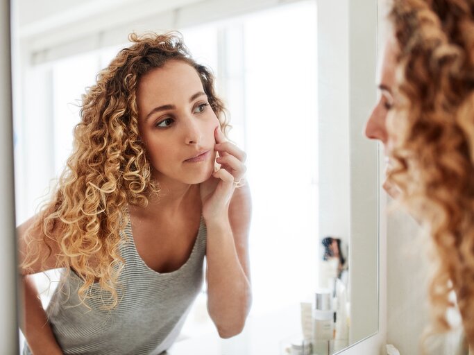 Frau blickt kritisch in den Spiegel | © Getty Images/LumiNola