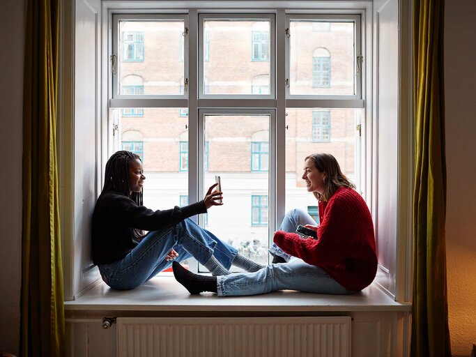 Junge Frau zeigt Freundin etwas auf dem Smartphone | © Getty Images/Klaus Vedfelt