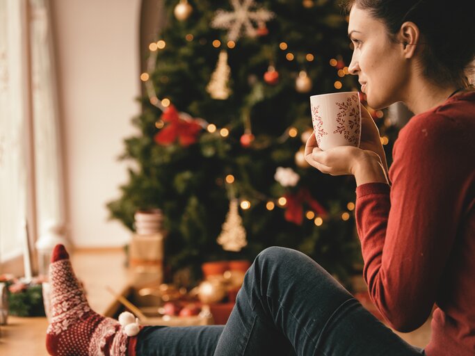 Junge Frau sitzt gemütlich unter dem Tannenbaum | © Getty Images/	fotostorm