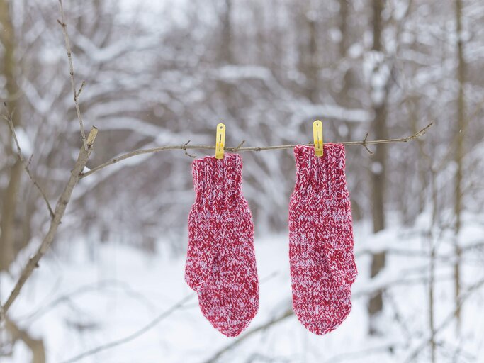 Handschuhe hängen bei Schnee auf der Wäscheleine draußen  | © Getty Images/sitnichonok