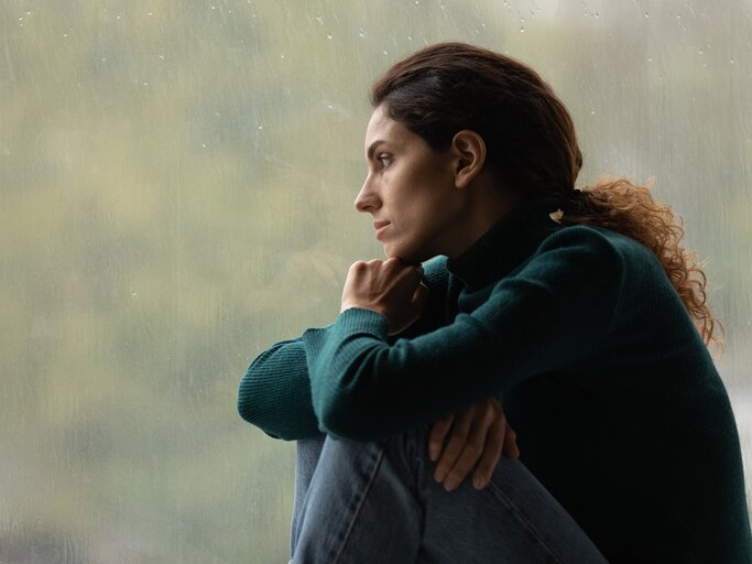Traurige Frau blickt aus dem verregneten Fenster | © Getty Images/	fizkes