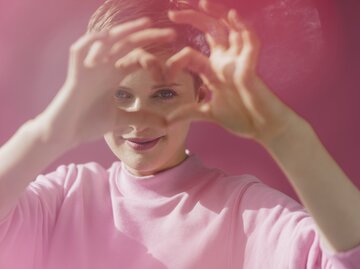 Frau formt mit ihren Händen ein Herz, rosafarbener Hintergrund | © Getty Images/	Westend61