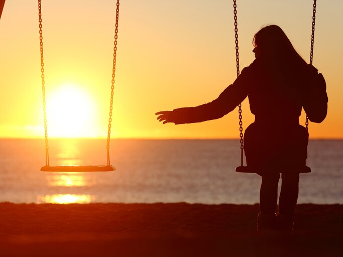 Frau sitzt alleine auf der Schaukel im Sonnenuntergang | © Getty Images/AntonioGuillem