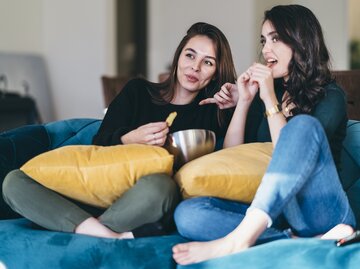 Zwei Frauen sitzen auf der Couch, gucken Fernsehen und essen Popcorn | © Getty Images/	recep-bg