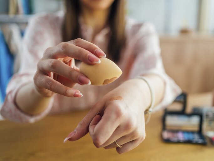 Frau benutzt Make-up-Ei auf ihrer Hand | © Getty Images/	LordHenriVoton