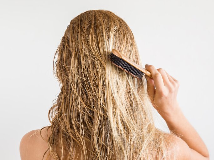 Frau mit blonden Haaren kämmt sich die Haare | © Getty Images/	FotoDuets