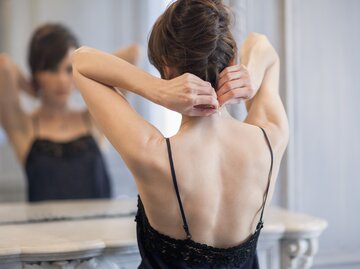 Frau zieht sich Kette im Spiegel an | © Getty Images/Letizia Le Fur
