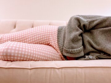 Frau liegt mit Periodenschmerzen im Bett | © Getty Images/Catherine McQueen