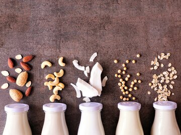 Milchflaschen über denen Mandeln, Haferflocken und Co. liegen | © GettyImages/jenifoto