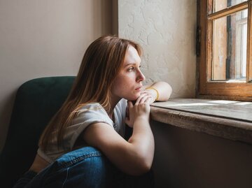 Person sitzt traurig vor Fenster. | © Getty Images/MementoJpeg